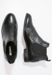 Sorte læder ankelstøvler med elastiske sidepaneler, dekorativ brogue-detaljering og en lav hæl, der har en glat finish og klassisk form.