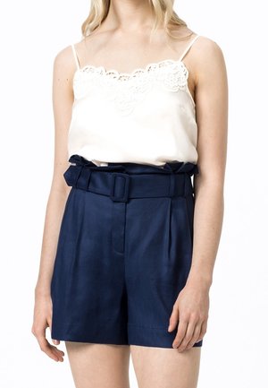 Witte satijnen cami met kanten rand, gecombineerd met marineblauwe shorts met hoge taille, een ceintuur en verborgen zakken.