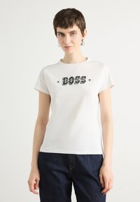 Balta medvilninė marškinė su trumpomis rankovėmis ir apvaliu iškirpimu, centre su juodu grafiniu užrašu "BOSS".