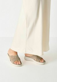 Beige sjal sandaler med leopardmönstrade remmar, texturerad tyg och en vadderad sula. Bärs med en krämfärgad golvlång klänning.