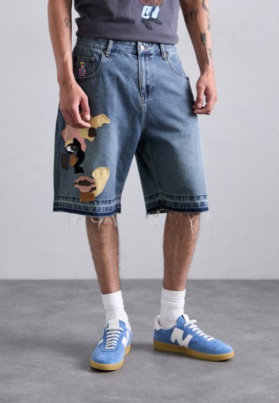 Shorts din denim de culoare albastră deschisă, cu tiv rupt, decorate cu petice din material colorat și un design al buzunarului pe partea stângă, asortați cu adidași albaștri.