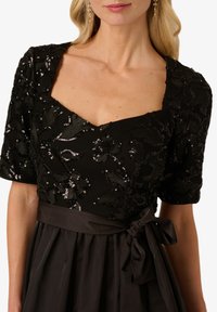 Czarna sukienka z kwadratowym dekoltem i bufiastymi rękawami, ozdobiona kwiatowymi cekinami na koronkowej części i satynowym paskiem w talii.