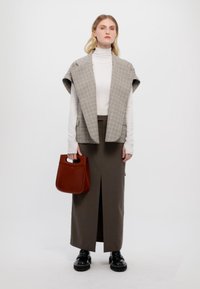 Grå rutig ärmlös blazer, vit polotröja, brun hög midjkjol med slits, svarta platåskor och en brun handväska.