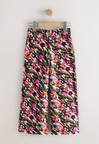 Wide-leg trousers with a multicolored leopard print in pink, green, orange, and cream. Made of smooth fabric, hung on a wooden clip.