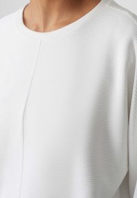 Witte textuur top met een ronde halslijn en subtiele horizontale strepen. De stof heeft een zachte, geribbelde uitstraling met minimale naden.