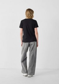 T-shirt nera a maniche corte, abbinata a jeans grigi larghi, con vestibilità rilassata e orlo sfrangiato. Modello di spalle contro uno sfondo semplice.
