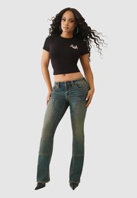 Czarny krótki top i niebieskie dżinsy z efektem sprania, kieszeniami z patkami oraz kontrastowym przeszyciem. Stylizowane z czarnymi butami na spiczastym nosku.