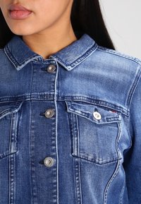 Denimjacka i medelblått med krage, silverfärgade knappar och två bröstfickor med en liten logotypdetalj.