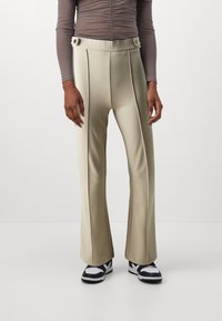 Beige vide bukse med glatt tekstur, med dobbeltknapp i livet og frontfold. Kombinert med svart og hvite sneakers.