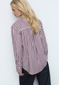 Chemise à manches longues rayée rouge et blanche avec un col boutonné, une coupe ajustée et un ourlet incurvé, en tissu lisse.