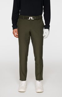 Oliwkowe spodnie golfowe o wąskim kroju, z przodu z zaszewkami i plecionym paskiem. Noszone z czarną bluzą z długim rękawem i białymi trampkami.