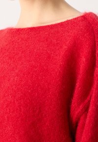 Area del collo e delle spalle che indossa un maglione a maglia rosso vivace e peloso con un ampio scollo.