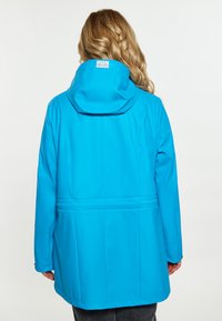 Cappotto blu resistente all'acqua con cappuccio, presenta una vita arricciata, una texture liscia e un'etichetta nella parte posteriore del collo.