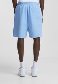 Shorts en coton bleu clair avec une taille élastique, des poches latérales et une poche arrière unique ; associés à des baskets blanches et des chaussettes.