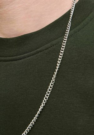 Grön bomullströja med ribbad halsringning, med ett glänsande silverhalsband mot en texturerad tygbakgrund.
