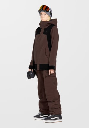 Brown ski jacket with black accents, matching brown pants. Features include zippers, pockets, and a textured beanie with goggles.