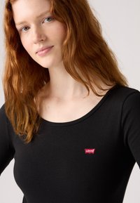 Svart langermet skjorte med rund hals; har en liten rød Levi's-logo på brystet; myk tekstur, tettsittende design.