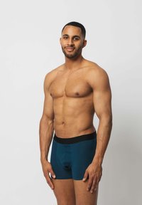 Dunkelblaugrüne Boxershorts mit schwarchem Bund, ausgestattet mit einem taillierten Design und weichem Material, präsentiert von einem Modell vor einem schlichten Hintergrund.