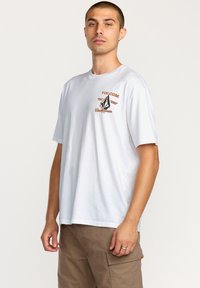 T-shirt en coton blanc avec un logo graphique sur la poitrine. Manches courtes et coupe décontractée. Texture lisse avec un col rond.