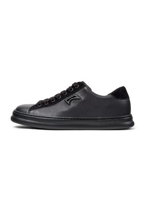 Zapatilla de deporte de cuero negro con una textura suave, punta redondeada, cordones negros, cuello acolchado y un logotipo sutil en el lateral.