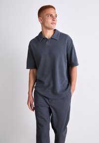 Mørk grå kortermet polo skjorte med flat krage og strukturert stoff, kombinert med matchende grå bukser med avslappet passform.