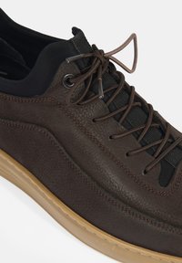 Chaussure en cuir marron avec une surface texturée, accents en tissu noir et lacets marron. Présente une semelle en gomme et des détails brodés.
