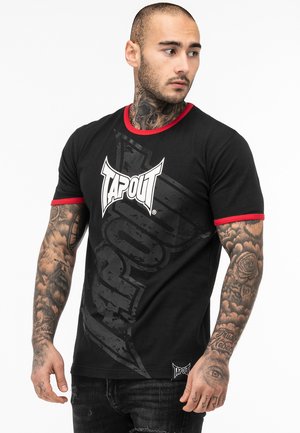 Melna īsām piedurknēm t-krekls ar sarkanu apdari, uz kura ir liels baltas krāsas "TAPOUT" logo un grafiskais dizains, izgatavots no mīksta kokvilnas auduma.