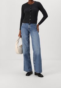 Cardigan côtelé gris foncé avec fermeture à boutons, associé à un jean large bleu clair. Accessoirisé d'un sac doux de couleur crème. Chaussures noires.