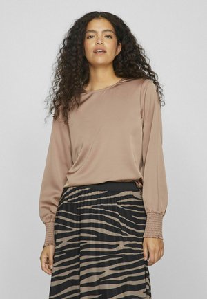 Langarm-Beige Bluse aus glattem Stoff, kombiniert mit einem schwarzen Rock mit auffälligem Zebra-Muster und gerafftem Ärmelabschluss.