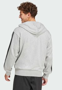 Sivý mikina s kapucňou a čiernymi bočnými pruhmi, vyrobená z mäkkej tkaniny, s voľným strihom a rebrovanými manžetami a spodným lemom.