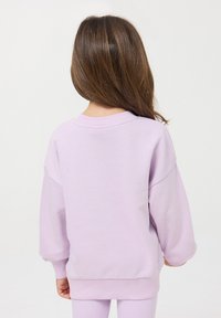 Jasnofioletowa bluza z ściągaczami przy mankietach i dole, o luźnym kroju i opadających ramionach. Miękki, bawełniany materiał w mieszance.