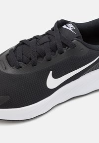Chaussure de sport noire avec un dessus texturé, des lacets noirs et le logo swoosh blanc de Nike. La semelle est blanche avec des détails subtils et une texture antidérapante.