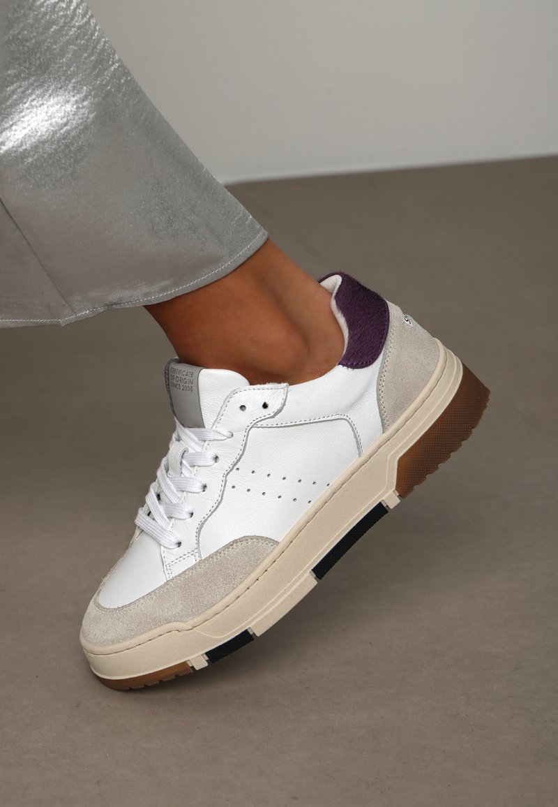 White leather sneaker with gray suede accents, purple heel, and a cream-colored sole featuring a textured, dark stripe along the edge.