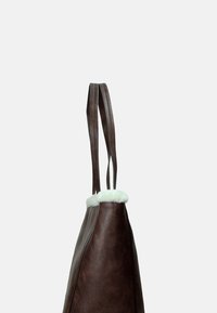 Borsa tote in pelle marrone con rifiniture in pelliccia bianca, forma allungata, doppi manici e superficie liscia. La vista laterale mette in risalto i dettagli del design.