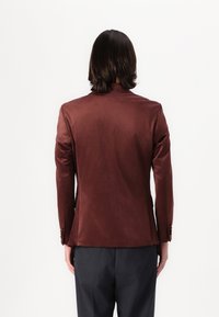 Blazer burdeos con textura suave, hombros estructurados y silueta elegante. Presenta un cierre de dos botones y un ajuste entallado.