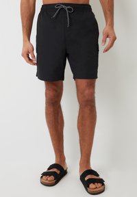 Czarne kąpielówki z elastycznym paskiem w talii i sznurkiem do regulacji. Posiadają boczne kieszenie i prosty krój. Połączone z czarnymi klapkami.