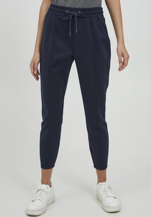 Námořnické jogger kalhoty s elastickým pasem a šňůrkou. Měkká, hladká látka s užšími nohavicemi. Model má na sobě bílé tenisky.