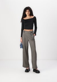 Černý dlouhý rukáv crop top, vysoké kostkované kalhoty s dvěma knoflíky a černé robustní boty; drží modrou kabelku.