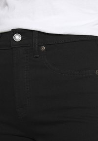 Vaqueros de denim negro con un corte ajustado, diseño clásico de cinco bolsillos, herrajes de botón plateado y detalles de costura en contraste.