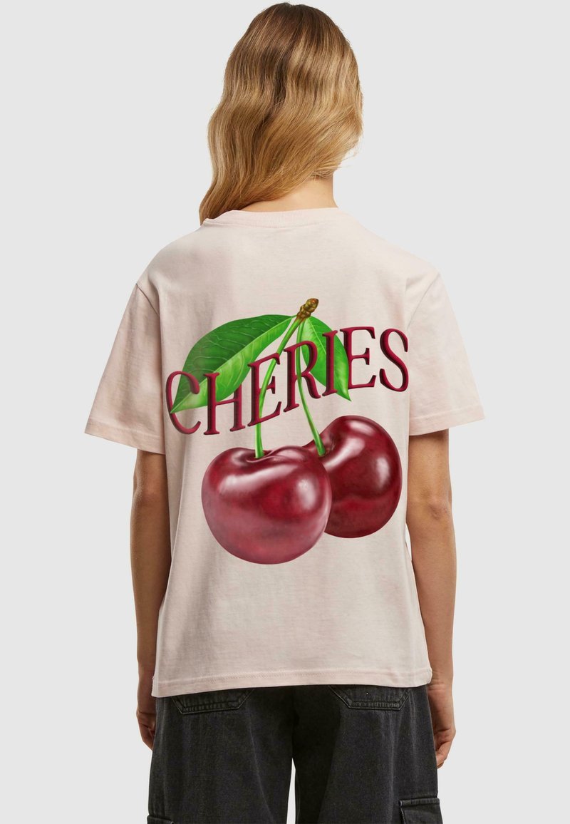 Heled roosa t-särk, millel on suur graafika kahe punase kirsiga roheliste lehtedega ja sõna "CHERIES" burgundia värvi kiri.