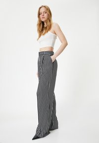 Zwart-witte gestreepte wide-leg broek met een hoge taille, zijzakken en een soepele stoftextuur. Puntige zwarte schoenen zichtbaar.