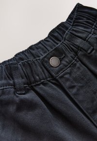 Pantalon en denim noir avec taille élastique, texture lisse et bouton en métal gravé de "nineteen eighty".