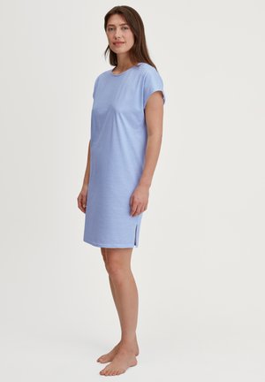 Donna in piedi a piedi nudi, che indossa un vestito a strisce blu e bianche, corto e lungo fino al ginocchio, con una piccola apertura laterale.