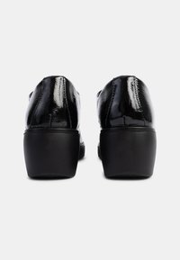 Schwarze Lacklederschuhe mit abgerundeter Spitze und niedrigem Blockabsatz, die ein glattes, glänzendes Finish und subtile Nahtdetails aufweisen.