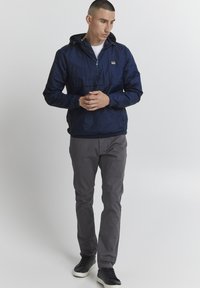 Veste à capuche navy avec une demi-fermeture éclair, des poignets élastiques et une poche frontale. Associée à un pantalon gris et des baskets noires. Tissu lisse et léger.