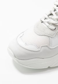 Baskets blanches avec un mélange de cuir lisse et de mesh sur la partie supérieure, des accents texturés, un col rembourré et une semelle en caoutchouc épaisse.