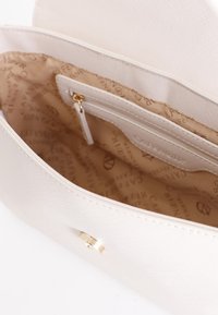 Interno di una borsa beige texturizzata con una tasca con cerniera dorata e fodera stampata con logo. Esterno liscio e dettaglio di chiusura a scatto.