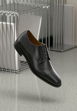 Black leather dress shoe with a polished finish, lace-up design, slightly pointed toe, and a low heel, set against a minimalist background.