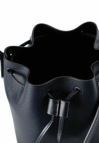 Borsa a secchiello in pelle blu navy con bordo scallopato, chiusura a coulisse e superficie liscia. L'interno è vuoto e foderato in tessuto scuro.