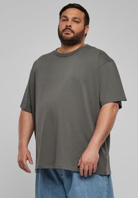Übergroßes graues T-Shirt aus Jersey-Material mit Rundhalsausschnitt, kurzen Ärmeln und geradem Saum, kombiniert mit hellblauen Jeansshorts.